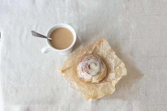 cup of coffee with milk and cinnamon roll with cream and spoon