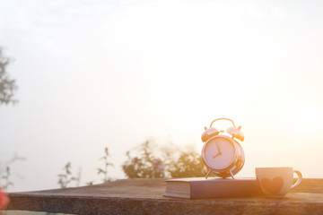 A white coffee cup and an alarm clock are placed beside the Bible on a wooden table in the morning...