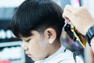 Asian boy is cut his hair in barber shop - people in hairdresser beauty salon concept