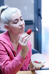 Blonde young woman standing at the kitchen while holding a strawberry