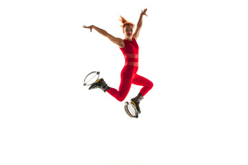 Fototapeta na wymiar Beautiful redhead woman in a red sportswear jumping in a kangoo jumps shoes isolated on white studio background. Jumping high, active movement, action, fitness and wellness. Fit female model.