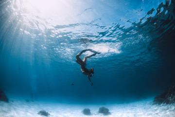 Freediver girl in bikini with fins glides underwater in blue transparent sea