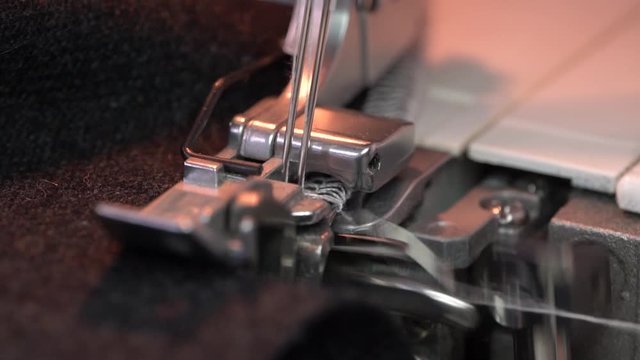 Overlock Sewing Machine. Close up stitches in slow motion. Machine serging the edges of fabric. Presser feet
