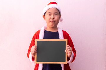 Asian boy in Santa Claus clothes holding empty board. Merry christmas