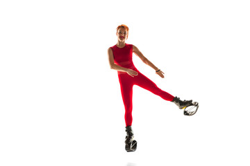 Beautiful redhead woman in a red sportswear jumping in a kangoo jumps shoes isolated on white studio background. Jumping high, active movement, action, fitness and wellness. Fit female model.