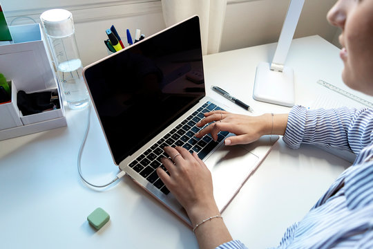 Top view of a young woman is typing on laptop keyboard over white office desk.