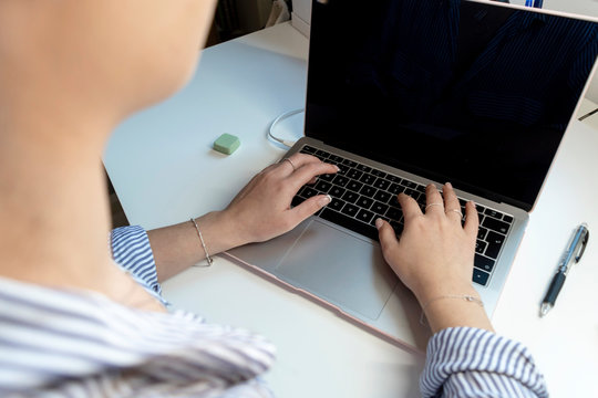 Top view of a young woman is typing on laptop keyboard over white office desk.