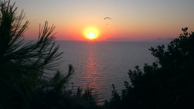 Man on a paraglider against the background of the sea and the setting sun.