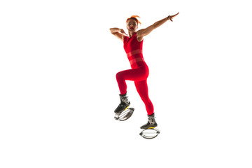 Beautiful redhead woman in a red sportswear jumping in a kangoo jumps shoes isolated on white studio background. Jumping high, active movement, action, fitness and wellness. Fit female model.