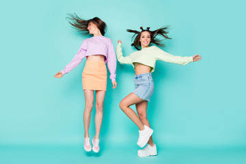 Full body photo of two pretty crazy ladies friends jump up youth clothes rejoicing dancing party wear cropped pullovers mini jeans skirts shoes isolated pastel teal color background