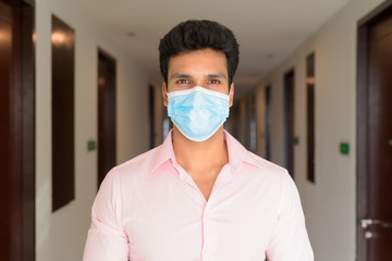 Face of young Indian businessman wearing mask for protection from corona virus outbreak in the corridor