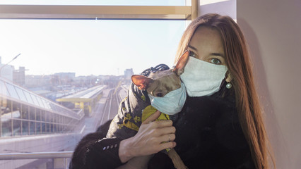Caucasian white woman with small dog wearing surgical medical mask at train station.