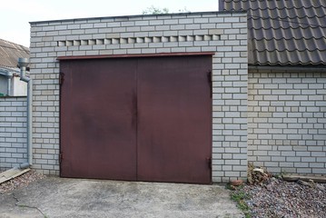 brown iron closed gate on a white brick wall of a private garage in the street on a sunny day