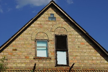 old brown brick loft of a rural house with a window and a door on a background of blue sky on a sunny day