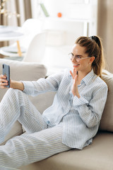 Online communication. Phone video call. Attractive young caucasian woman is communicate by a video conference by phone with her family while sitting at home on a couch in a positive mood