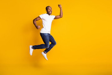 Fototapeta na wymiar Full size photo of attractive dark skin guy jumping high up rejoicing best win sports bets bookmaker wear casual white t-shirt jeans shoes isolated yellow color background