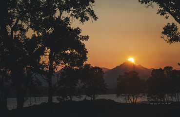 Beautiful bright orange sunset, the sun sets over the mountain, silhouettes of trees against the backdrop of mountains and the sea
