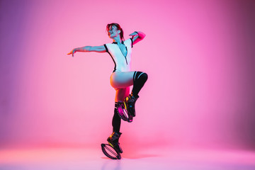 Beautiful redhead woman in sportswear jumping in a kangoo jumps shoes isolated on purple-pink...