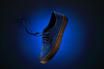 Close up view of levitation blue sneakers shoe with  flying laces over blue background with copy space for text. 