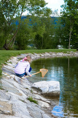 The child, a little girl with a net catches fish in the lake and walks.