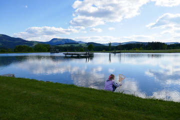 The child, a little girl with a net catches fish in the lake and walks.