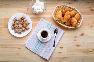 Cup of coffee on napkins on a wooden table with croissants and waffles.
