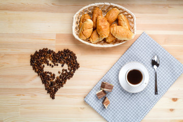 A cup of coffee on a napkin on a wooden table and a scattered jaundice of coffee in the shape of a heart.