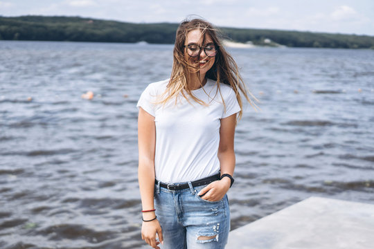 Portrait of a beautiful young woman in stylish glasses. Girl in white tshirt posing on the background of the lake landscape