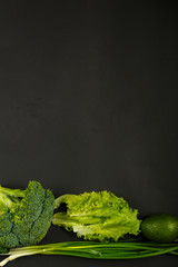 Green vegetables, broccoli, avocado, onions, spinach and salad on the edge of a black background.
