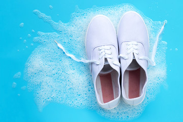Sneakers with foam of powder detergent water dissolution on blue background. Washing dirty shoes.