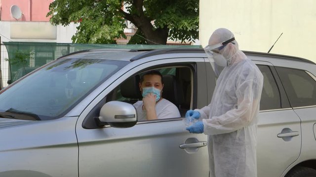 Medical worker in hazmat suit taking a swab sample from nose to a man in car seat
