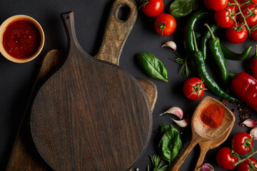 top view of cherry tomatoes, garlic cloves, tomato sauce, rosemary, peppercorns, and green chili peppers near chopping boards on black