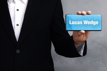 Lucas Wedge. Businessman holding a phone in his hand. Man present screen with word. Blue Background. Business, Finance, Statistics, Analysis, Economy