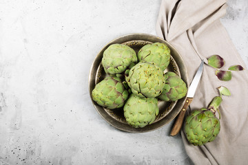 Pile of green Spanish or Italian Artichokes on the metal rustic plate and gray background. Top view with copy space