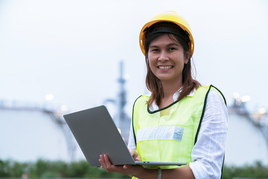 Close up engineer woman wearing work helmet and reflective vest,  using laptop while working at power plants.