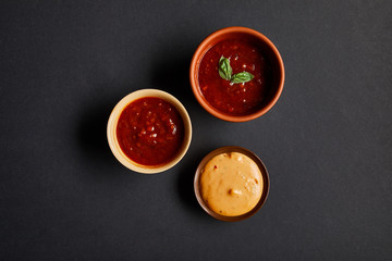 top view of bowls with tomato and mustard sauces on black