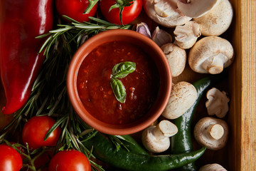 top view of tomato sauce with basil leaves near cherry tomatoes, green chili peppers, mushrooms and rosemary