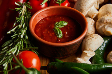 selective focus of tomato sauce with basil leaves near cherry tomatoes, green chili pepper, mushrooms and rosemary