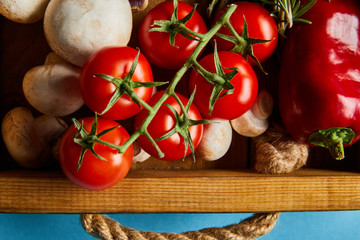 top view of mushrooms near red cherry tomatoes and chili pepper in wooden box on blue