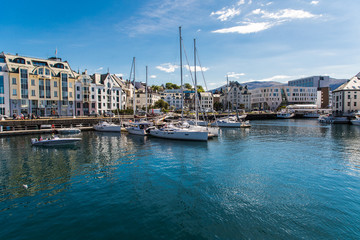 Fototapeta na wymiar Alesund, Norway - June 2019: View of colorful Art Nouveau architecture in the port of the city of Alesund, Norway. Panoramic view of Alesunds architecture and docked sailing boats and vessels.
