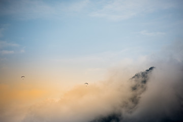 Fototapeta premium Paragliders flying over misty mountain range at dawn.