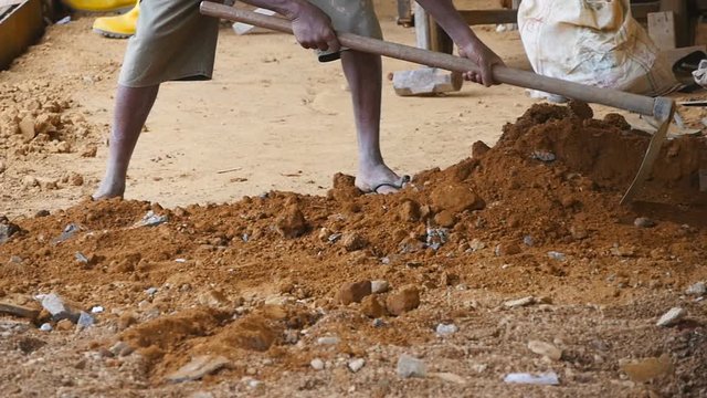 Low view of male indian hands rakes sand or ground with a hoe at building site. Local unrecognizable builder works on construction area. Concept of future project. Close up Slow motion