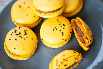 Macaroons on a plate on a gray background. French macarons isolated. Selective focus. Beautiful yellow macaroons with sesame. Stylish arrangement sweet. Flat lay, top view. Macro photo.