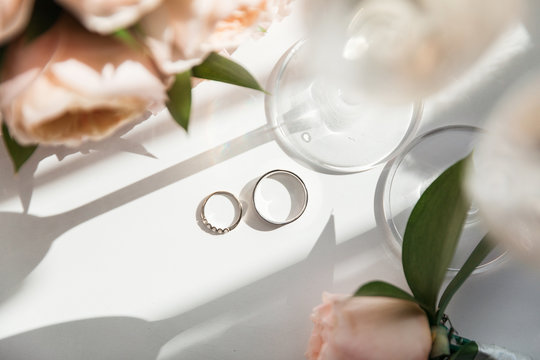 Wedding rings lie next to two glasses of champagne and a bouquet of roses in the sun