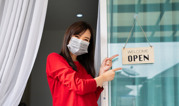 Woman wearing mask opening store with sign board front door shop for service customer, Small business turning agian after the situation is resolved.