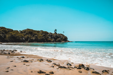 Beautiful secluded beach on an isolated island. Blue water and white waves spume on a sandy beach with stones in Sri Lanka. Escape to remote destination, relax and unwind near pleasant seashore.