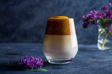 Summer still life with dalgona coffee in tall glass and lilac flowers on dark background. Instant...