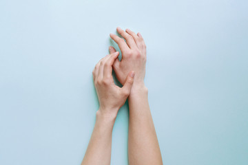 Tender female hands lie calmly on a light blue table.