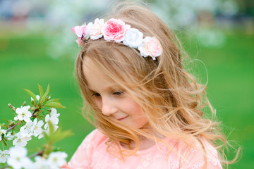 Pretty child girl smiling and playing in flowers of the garden, blooming trees, cherry, apples.