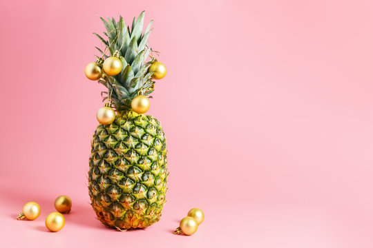  golden christmas balls on pineapple, pink background. pineapple like a christmas tree. Travel concept for christmas or new year. copy space, minimalism